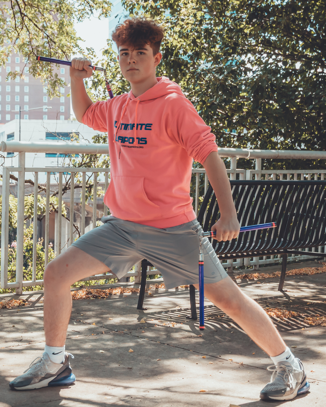 Person in pink hoodie and gray shorts holding a javelin outdoors
